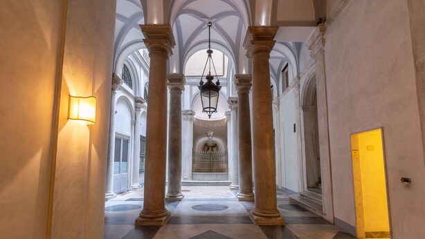 A grand hallway with high ceilings, large columns, and a central chandelier.