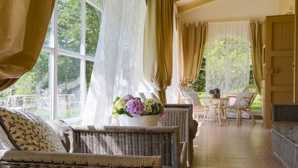 A sunlit room with wicker furniture, a table with a vase of flowers, and a view of greenery outside. - La Villa Dina 10, Emma Villas (Modigliana)