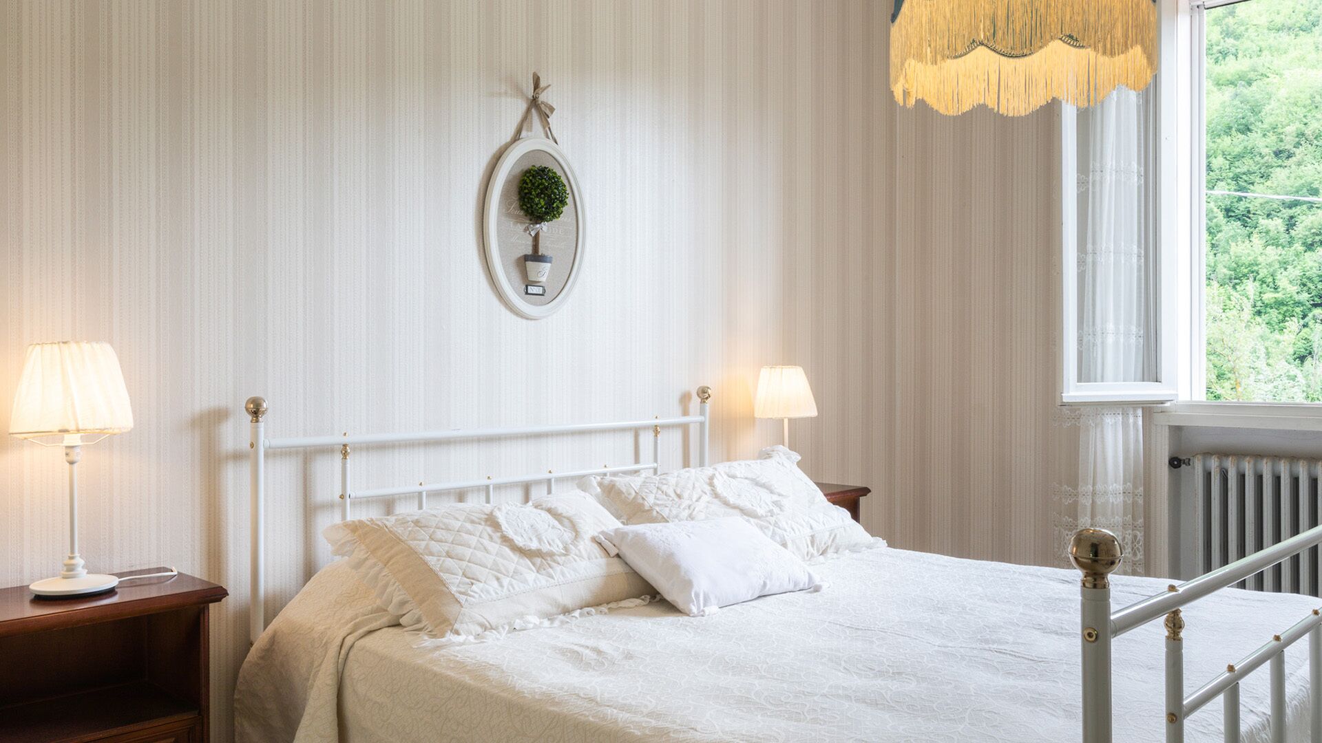 Cama bem arrumada com lençóis e almofadas brancas, uma decoração redonda na parede e duas luminárias de cabeceira.