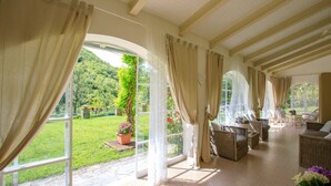 A spacious room with large windows, wicker furniture, and a view of a lush garden. - La Villa Dina 10, Emma Villas (Modigliana)
