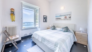 Un dormitorio con cama, mesita de noche, una silla, radiador, ventana y decoración en la pared.