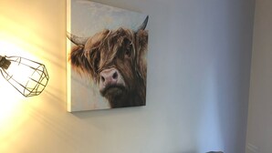 Una sala de estar con un sofá gris, varios cojines y un cuadro de una vaca en la pared.