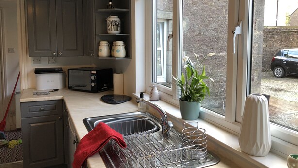 Una cocina compacta con microondas integrado, un panel para el pan y un escurreplatos.
