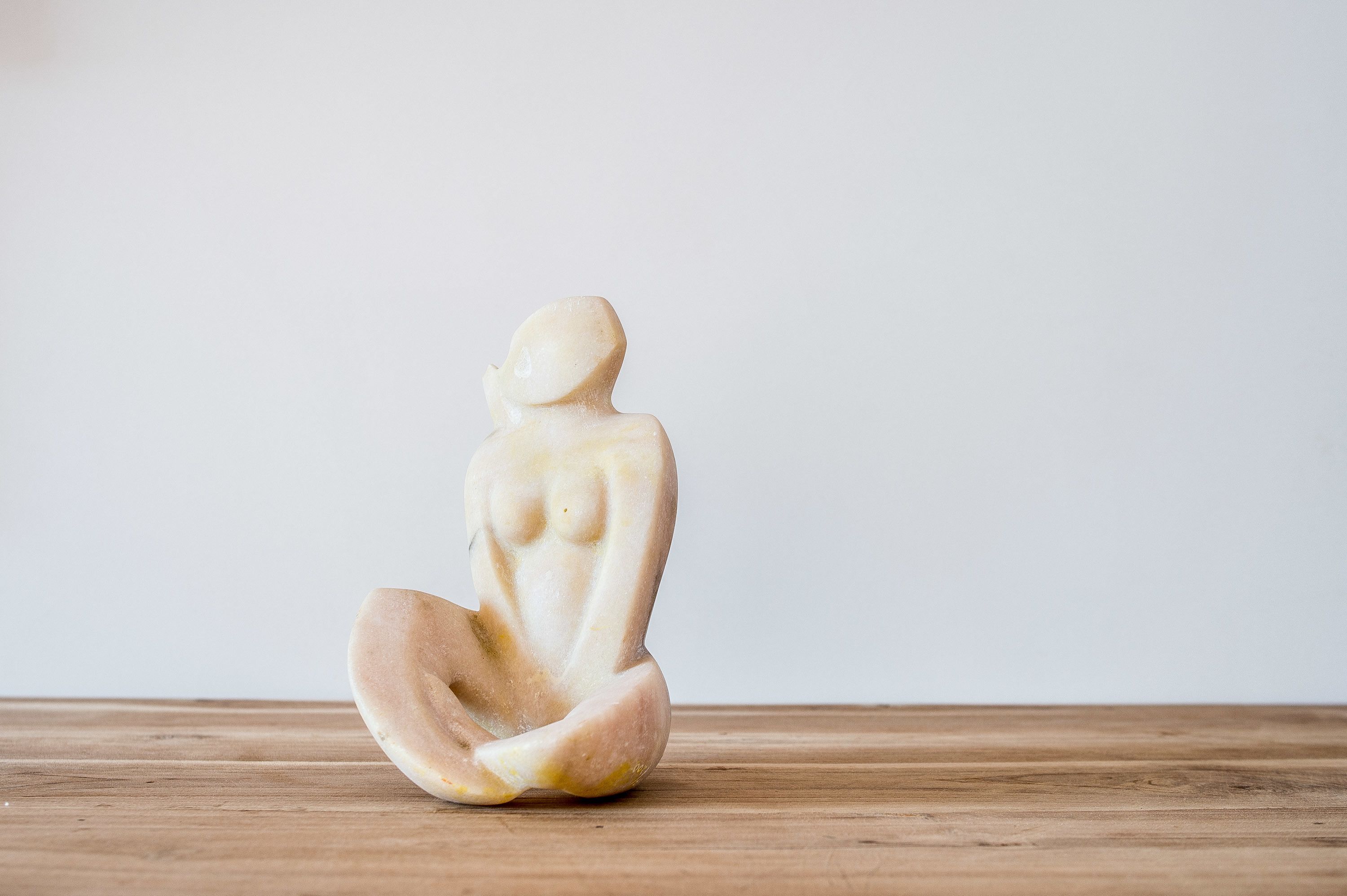 A small, abstract sculpture on a wooden surface against a plain background.