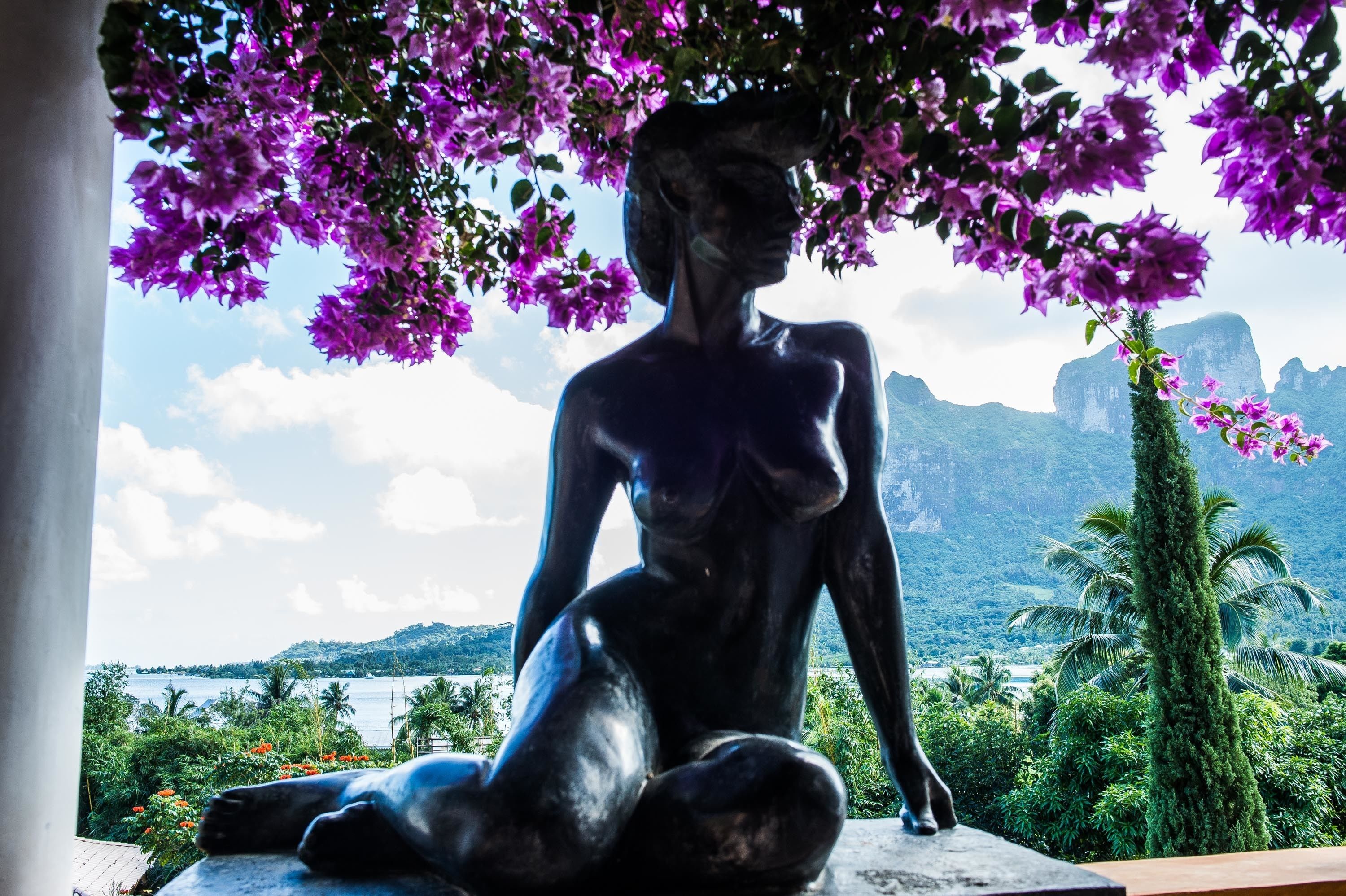 A statue of a seated figure with a backdrop of mountains and a body of water.