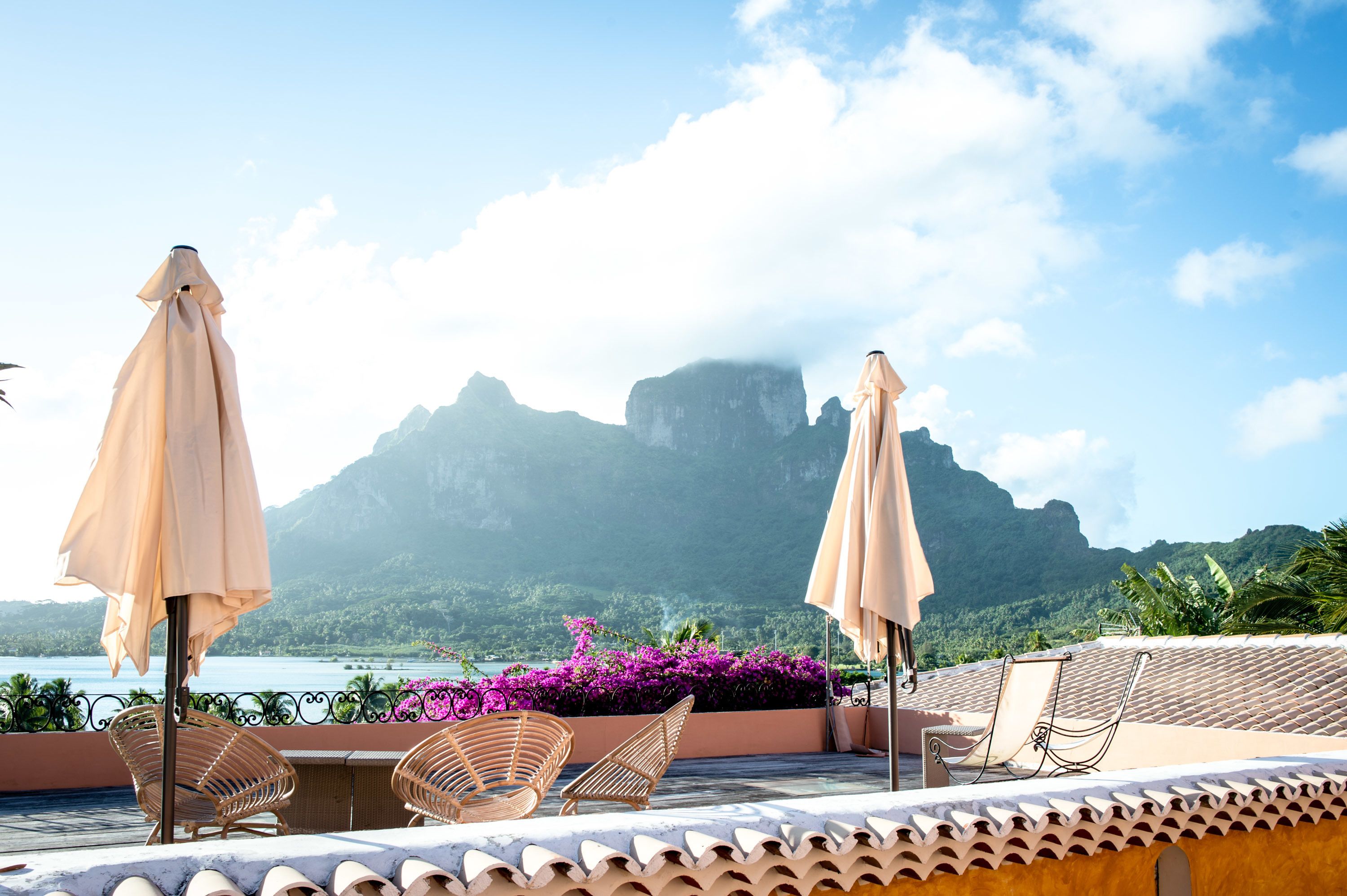 Une terrasse sur le toit, agrémentée de deux parasols beiges, de chaises en osier et offrant une vue sur une montagne et la mer.