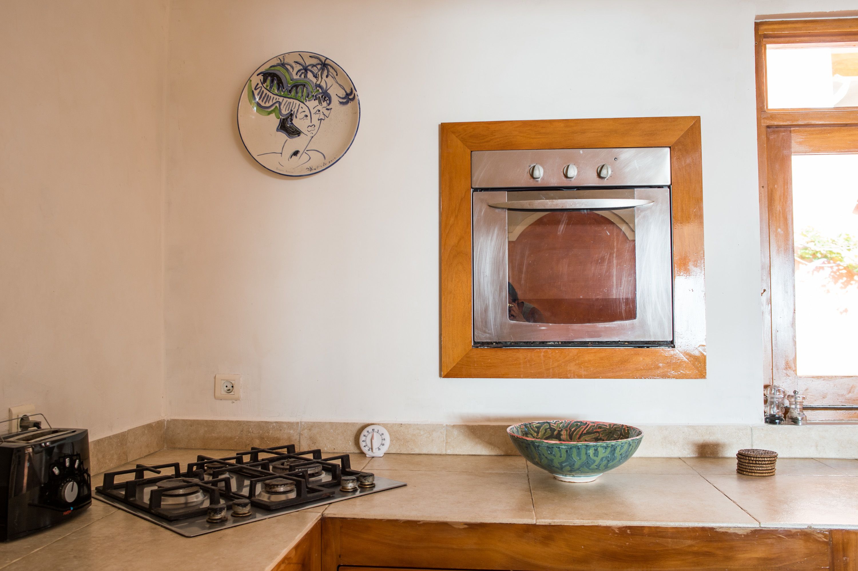 A kitchen with a gas stove, an oven, a decorative plate, and a window.