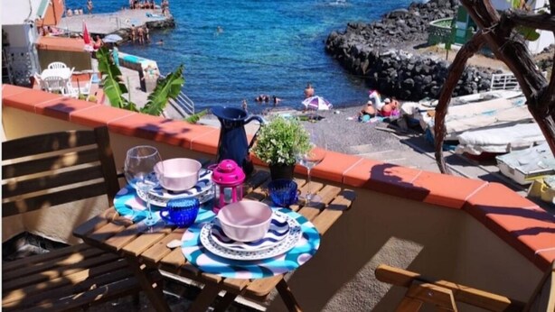 A terrace with a table set for dining, overlooking a rocky beach with people in the water. - Cosy house in small fishing village away of crowds (El Tablado, Güímar)