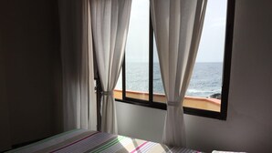 A bedroom with a bed, curtains, and a window overlooking the sea. - Cosy house in small fishing village away of crowds (El Tablado, Güímar)