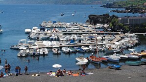 A marina with numerous boats docked, a beach area with people sunbathing, and a hilly landscape in the background. - Apartment with terrace with sea and Etna view (Stazzo)