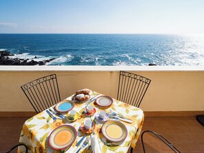 Een tafel gedekt met borden, kopjes en gebak op een balkon met uitzicht op de oceaan.
