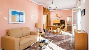 A living room with a beige sofa, a glass coffee table, a dining area with a wooden table and chairs, and a kitchen area with wooden cabinets and a sink. - Apartment with terrace with sea and Etna view (Stazzo)