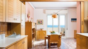 A kitchen with wooden cabinets, a dining table with chairs, and a view of the sea through a glass door. - Apartment with terrace with sea and Etna view (Stazzo)