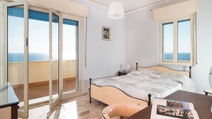 A bedroom with a bed, a desk, a chair, a lamp, and a view of the sea through the windows. - Apartment with terrace with sea and Etna view (Stazzo)
