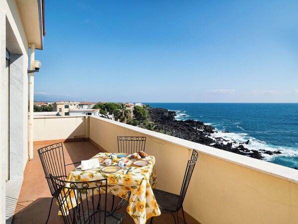 A balcony with a table set for two, overlooking a rocky coastline and the sea. - Apartment with terrace with sea and Etna view (Stazzo)