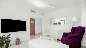 Een moderne woonkamer met een witte bank, een paarse fauteuil, een flatscreen televisie, een salontafel en een potplant.
