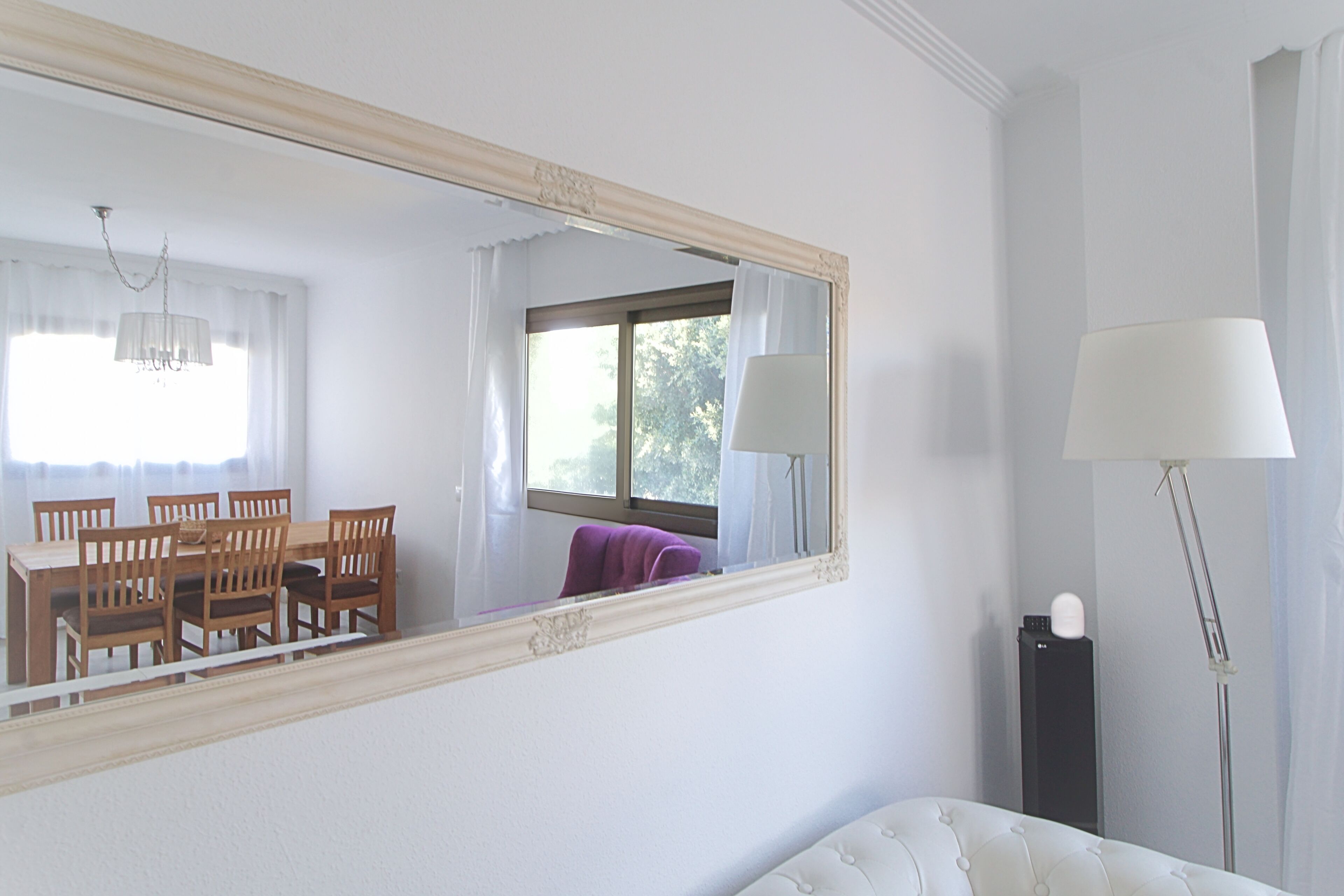 A hotel room with a dining table and chairs, a large mirror, a bed, and a floor lamp.