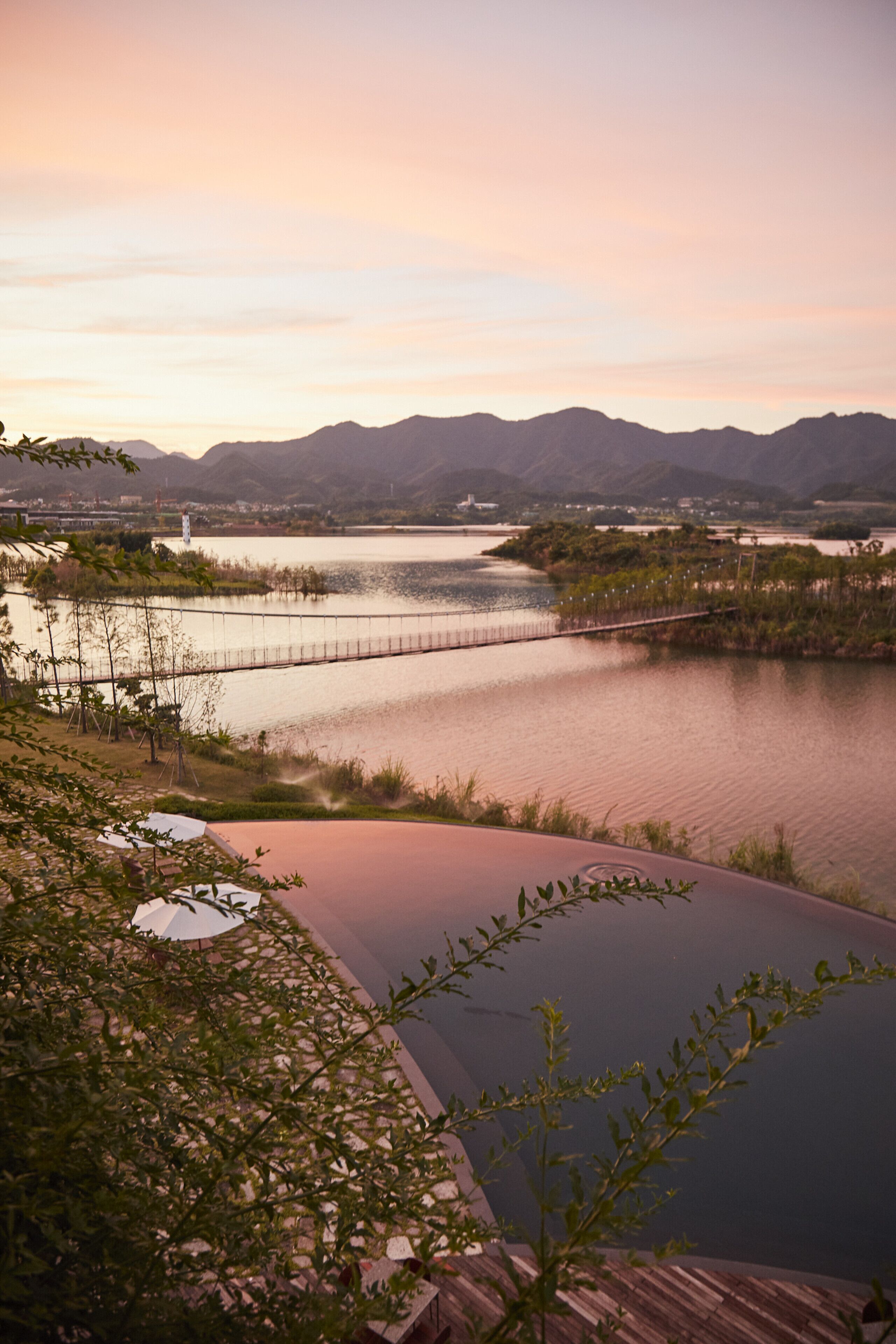 A serene lakeside view with a wooden deck, a bridge, and distant mountains.