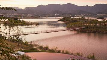 A serene lakeside view with a wooden deck, a bridge, and distant mountains.