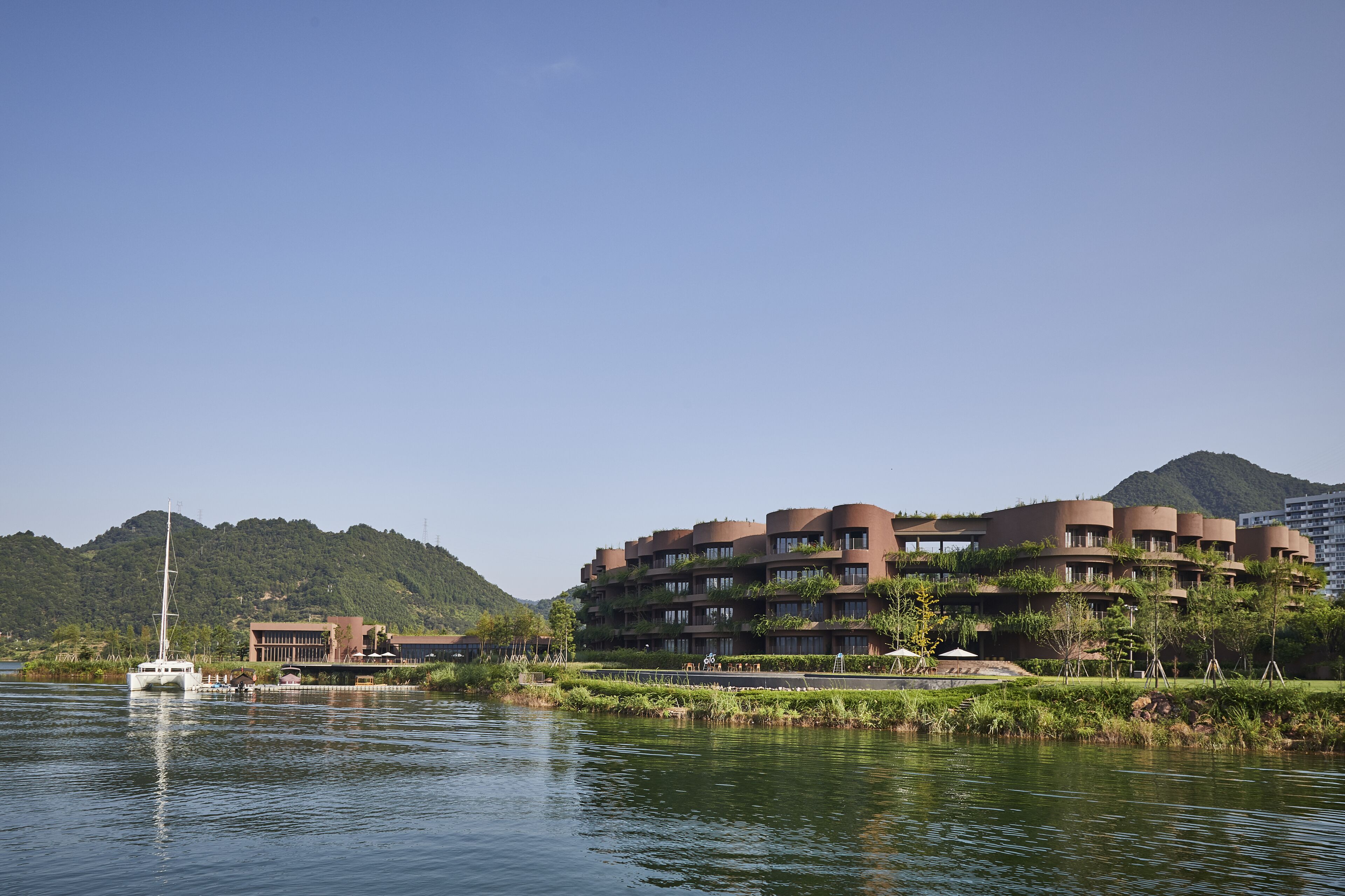 Ein modernes Hotel mit Blick auf das Wasser, inklusive Bootsanleger und üppiger Bepflanzung.