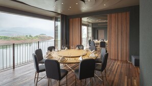 Un salón de conferencias con una mesa redonda, sillas y vistas a un río y montañas.
