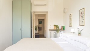 Une chambre avec un lit, une armoire, un radiateur et des œuvres d’art encadrées accrochées au mur.