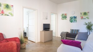 Un salon moderne avec un canapé, un téléviseur posé sur un meuble et des œuvres d’art aux motifs tropicaux accrochées aux murs.