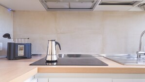 Une cuisine moderne avec une bouilloire en acier inoxydable posée sur une plaque de cuisson à induction noire, un évier encastré et un pare-feu de couleur claire.
