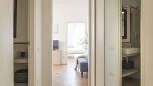 Un couloir mène à un espace de vie comprenant un canapé, un téléviseur et une plante.