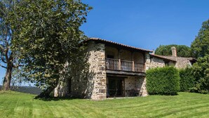 A stone building with a balcony, surrounded by greenery and a clear blue sky.