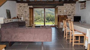 A rustic interior with a stone wall, wooden furniture, and a large window offering a view of the outdoors.