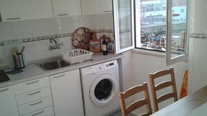 A compact kitchen with a washing machine, a sink, and a window with a view of a building.
