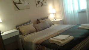 A neatly made bed with pillows and a folded towel, a bedside lamp, and artwork on the wall.