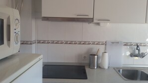 A kitchen with white cabinets, a microwave, a sink, and a black mat on the counter.