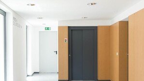 A modern hallway with a central elevator, a door with an emergency exit sign, and a glass wall on one side. - Central Lisbon - Downtown | AC | Wi-Fi | Elevator & Garage (Lisboa)