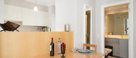 A modern kitchen with white cabinets, a wooden dining table, and a hanging light fixture.