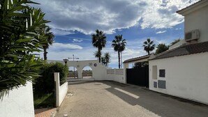 A gated entrance with a white wall, palm trees, and a clear sky.