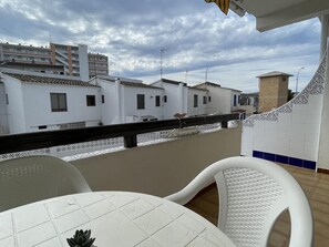 Un balcon doté d’un sol carrelé de carreaux blancs, de chaises blanches et offrant une vue sur des bâtiments blancs aux toits bruns.