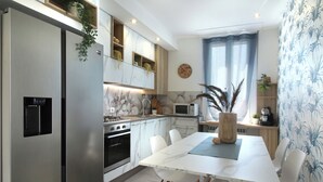 Una cucina moderna con frigorifero in acciaio inossidabile, forno integrato e microonde. Si vede un tavolo da pranzo con sedie e un vaso con piante.