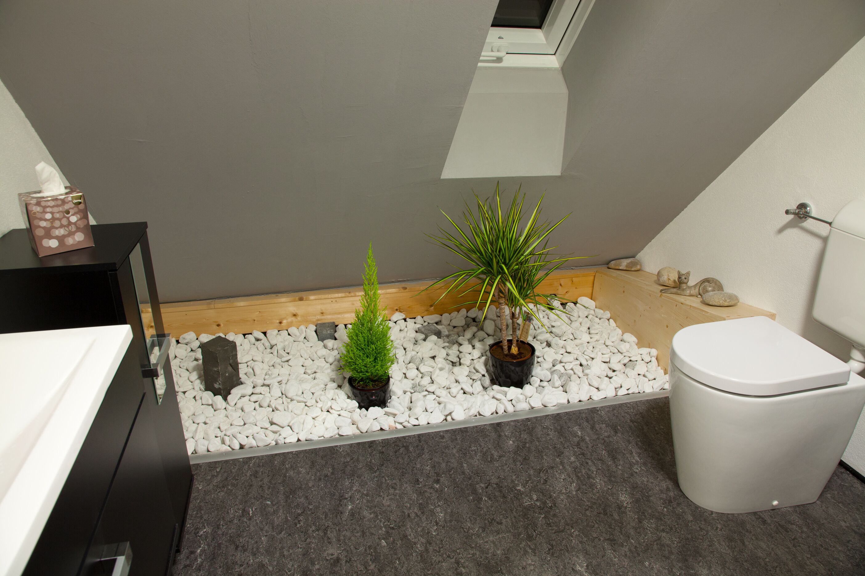 A bathroom with a toilet, a sink, a small potted plant, and a tissue box on a black side table.