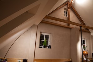 A room with a sloped ceiling, wooden beams, a small window with a plant, and a lamp. - Stylish cozy gable suite in the former bakery in Fulda (Fulda)