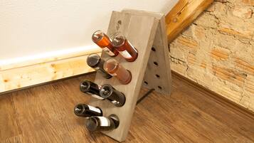Un meuble à bouteilles, avec des bouteilles de vin, est placé dans un coin d’une pièce dont le sol est en bois et un des murs est en briques.