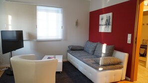 Ein modernes Wohnzimmer mit einem weißen Sofa, einem weißen Sessel, einem kleinen Tisch und einem Flachbildfernseher.