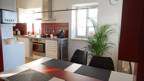 Eine kompakte Küche mit Mikrowelle, Herd und Backofen, ein Esstisch mit Platzdeckchen und ein großes Fenster mit Blick nach draußen.