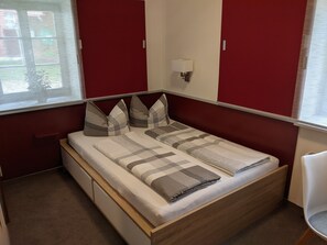 Ein ordentlich bezogenes Bett mit gestreifter Bettdecke und Kissen, ein Nachttisch und eine Wandlampe.