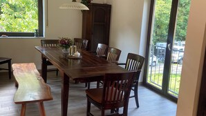 Un comedor con una mesa de madera, sillas y un banco. Hay una lámpara en el techo y una ventana con vistas a zonas verdes.