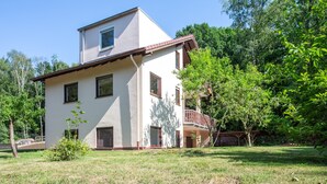 Una casa de dos pisos con balcón, rodeada de follaje.