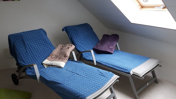 Deux fauteuils de massage bleus, accompagnés d’une serviette et d’un coussin violet, se trouvent dans une pièce dotée d’un plafond en pente et d’une lucarne.