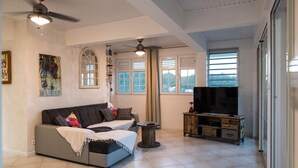 A living room with a sofa, TV, and a ceiling fan. - Superb views - Private spa, pool and pool house. Romanticism and luxury -Trois Ilets.  (les Trois Ilets)