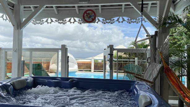A hot tub with a view of a pool and slides, a no shoes sign, and a covered area with a white ceiling and decorative elements. - Superb views - Private spa, pool and pool house. Romanticism and luxury -Trois Ilets.  (les Trois Ilets)